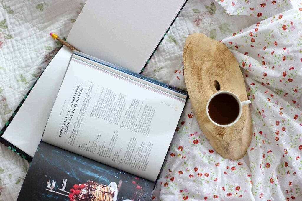 Kochbuch auf dem Bett mit einer Tasse Kaffee aufgeschlagen - Ratgeber für Kochbuchgeschenke